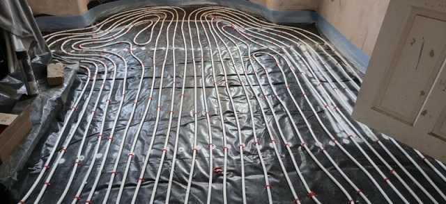 A floor with white pipes arranged on a black surface, some covered with plastic sheeting.