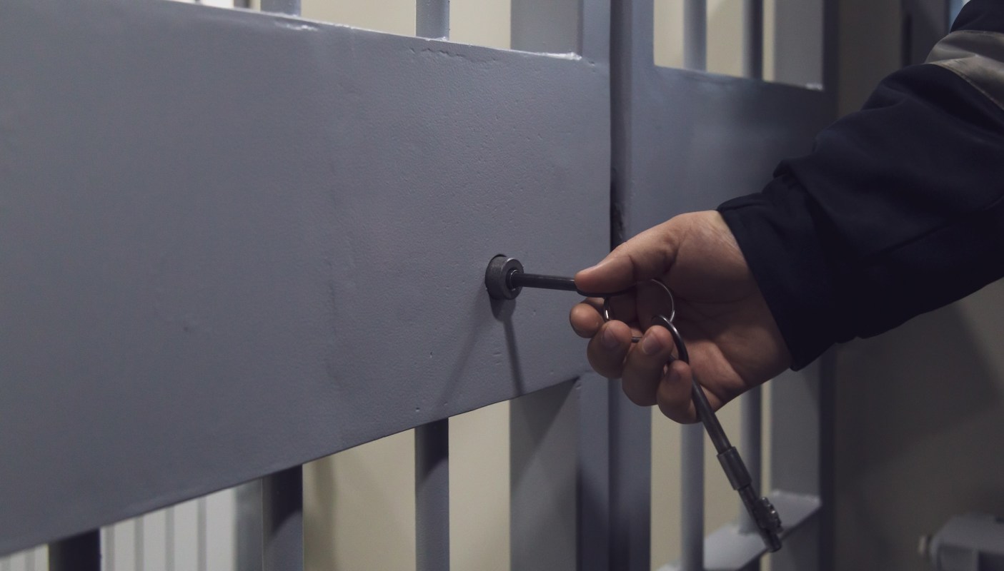 A hand inserting a key into a lock on a gray metal gate.