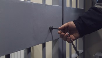 A hand inserting a key into a lock on a gray metal gate.