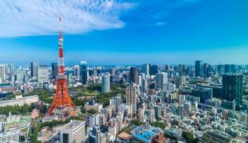 Tokyo Tower stands prominently amidst a cityscape filled with modern buildings and green spaces under a clear blue sky.