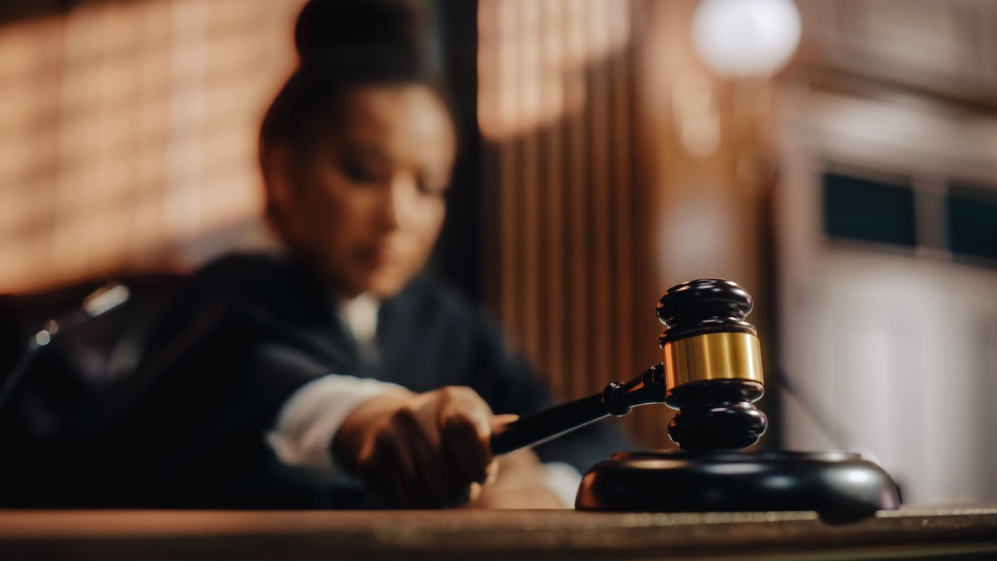 A judge's gavel is positioned on a desk in a courtroom setting.