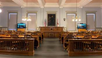A historic courtroom with wooden furniture, American and Florida flags, and a television displaying a black-and-white image.