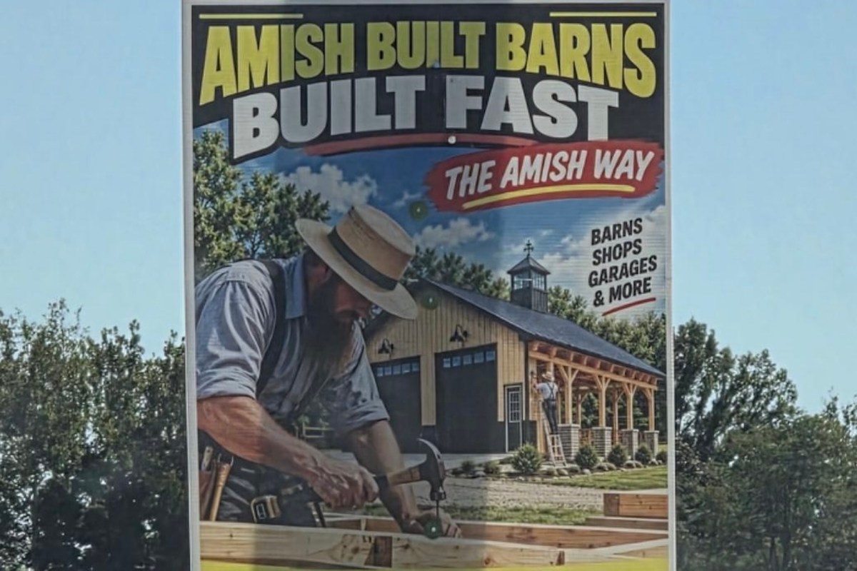 A promotional sign featuring an Amish carpenter building a barn with text announcing fast construction services.