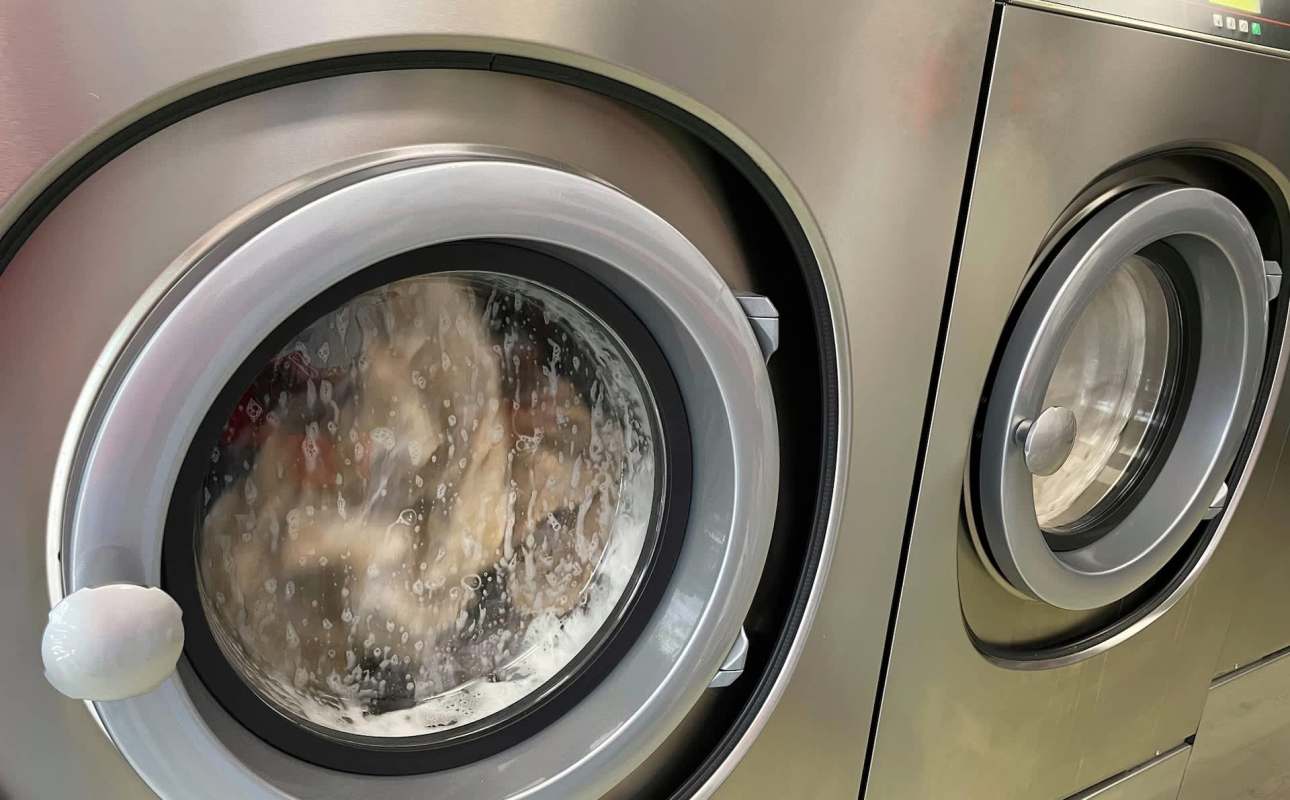Two washing machines, one filled with soapy water and laundry, the other empty with a clear glass door.