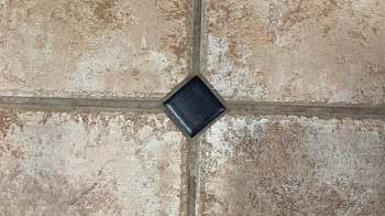 A black square tile on a textured ceramic floor.