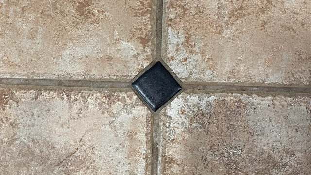 A black square tile on a textured ceramic floor.