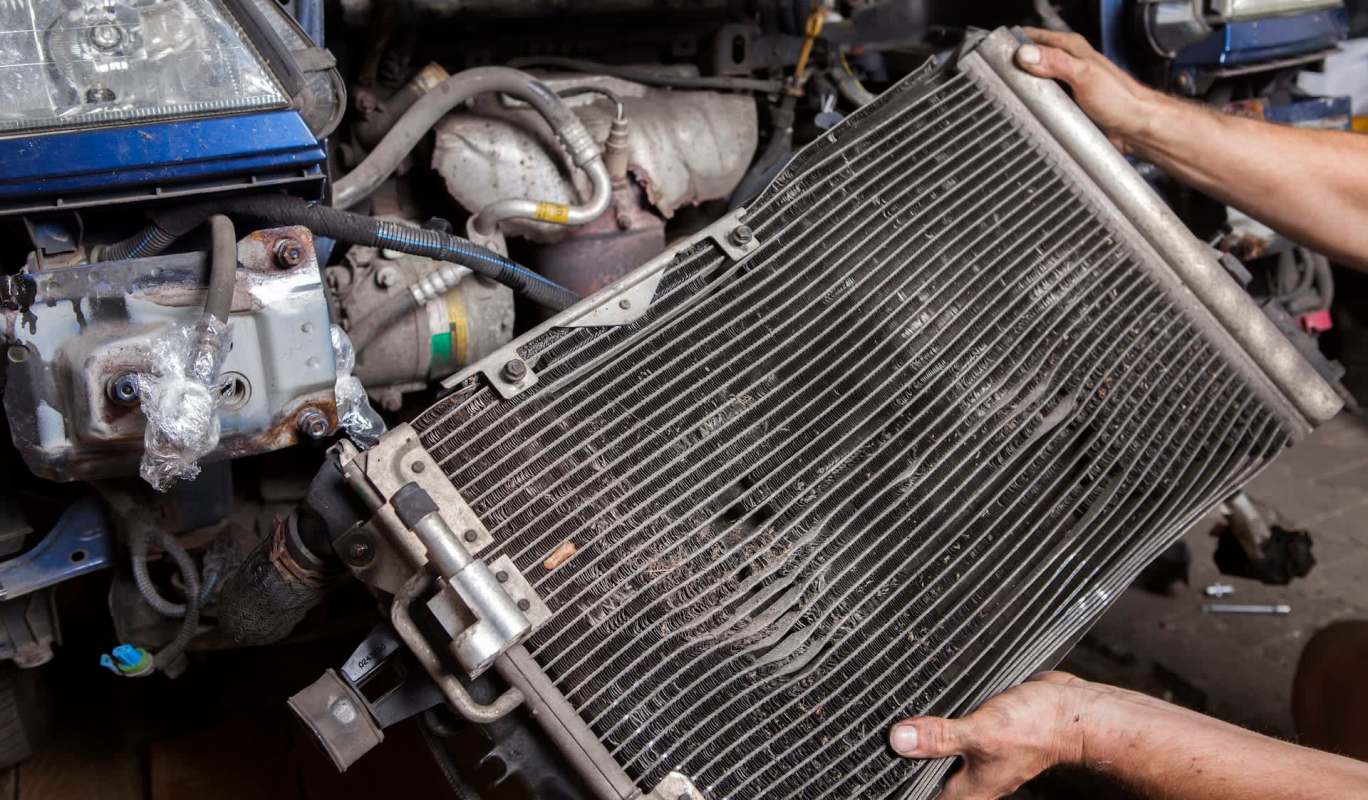 A person holds a dirty car radiator while working on an engine.