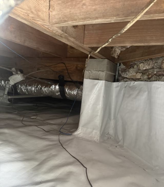 An indoor space with a white plastic vapor barrier, a pipe, and exposed wooden beams.