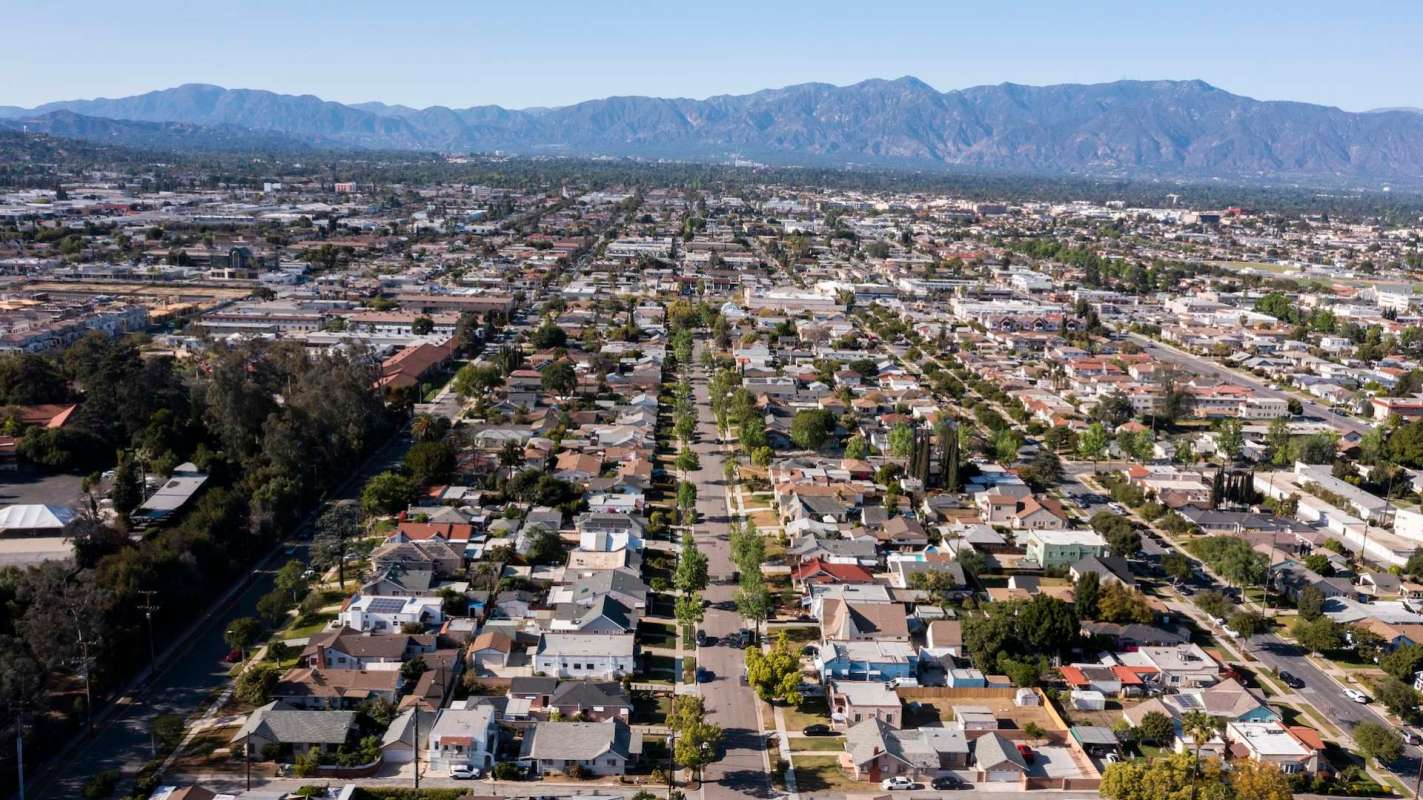 An aerial view of a suburban neighborhood with houses and streets, surrounded by mountains in the distance.