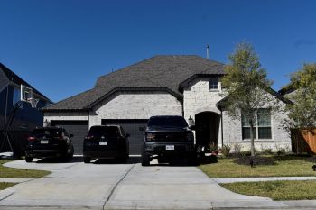 A modern house with a stone front, three parked black vehicles, and a basketball hoop in the driveway.