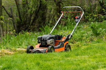 An orange lawnmower near tall grass.