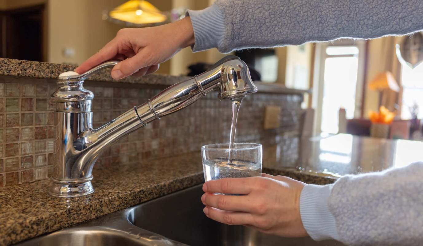 A person fills a glass with water from a kitchen faucet.