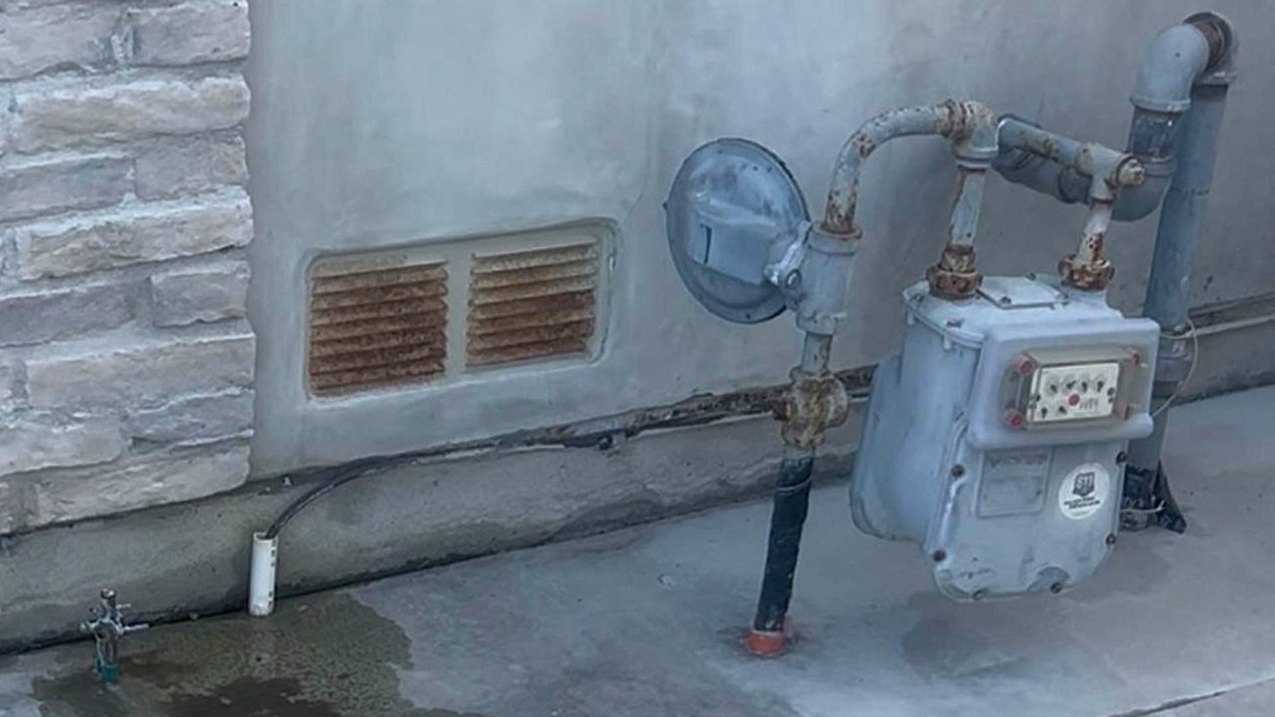A pipe system against a wall with a vent and a small faucet on the ground.