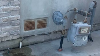 A pipe system against a wall with a vent and a small faucet on the ground.