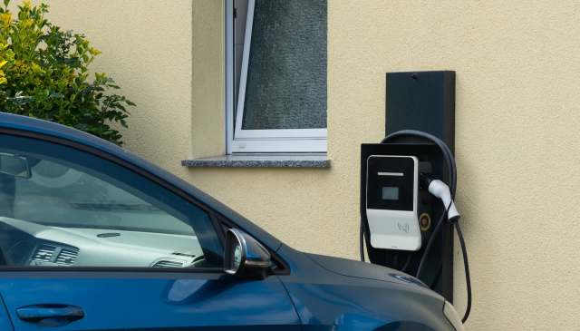 An electric vehicle charging station next to a car and a window on a yellow wall.