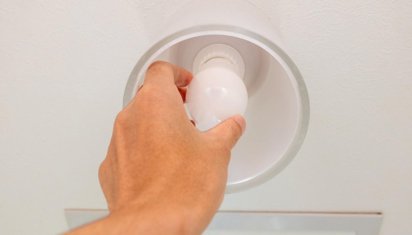 A hand installs a light bulb into a ceiling fixture.