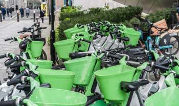 A row of green Lime bicycles with green baskets parked on a London street.