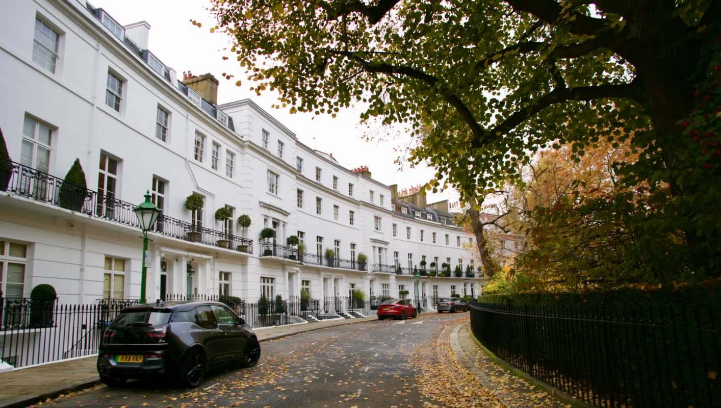 A tree-lined London street featuring white townhouses and parked cars.