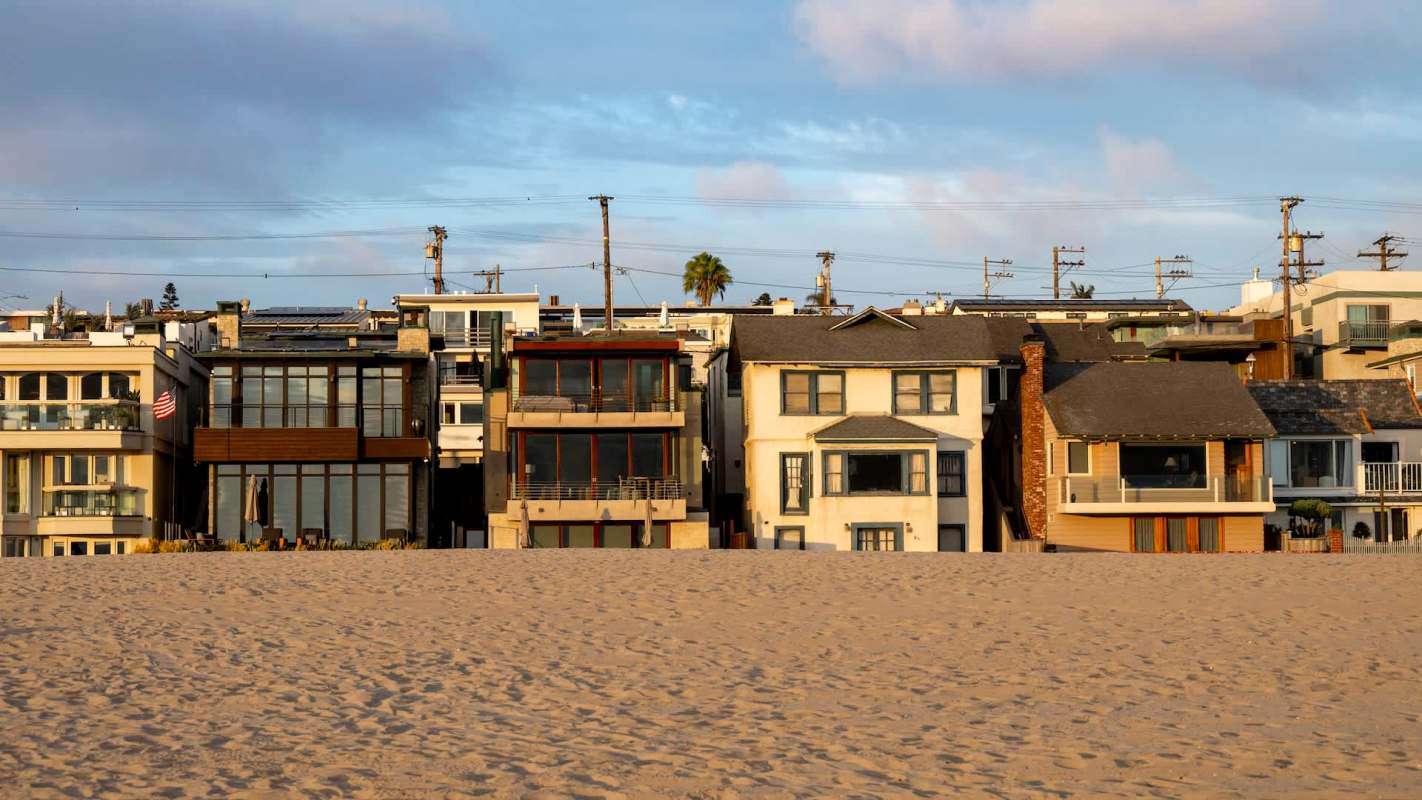 A series of beachside houses in California along a sandy shore with a clear sky.