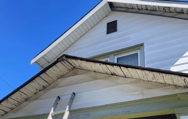A section of a house exterior with a ladder positioned against the wall under a blue sky.