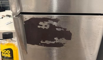 A bottle of Goo Gone in front of a magnet stuck on a fridge.