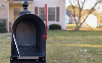 An open mailbox with a small piece of mail inside, set against a residential background.