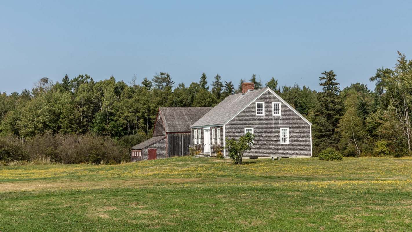 A white house and a red barn in a grassy field surrounded by trees.