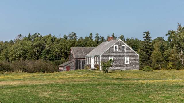 A white house and a red barn in a grassy field surrounded by trees.