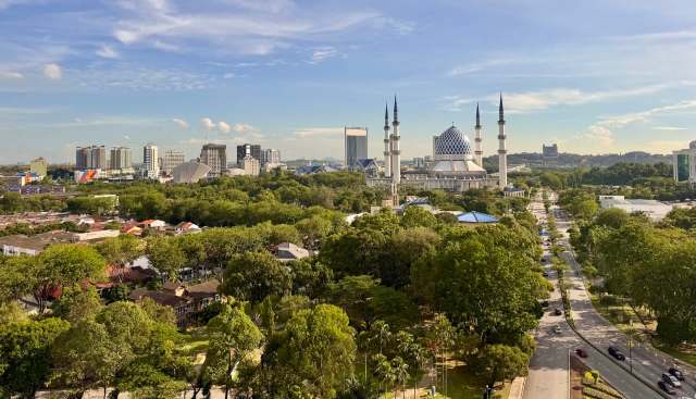 A view of a cityscape featuring a mosque, modern buildings, and greenery.
