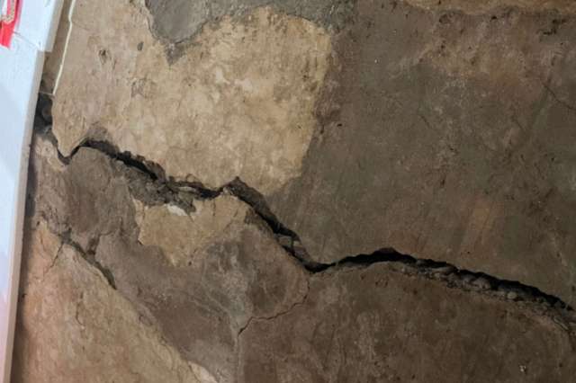 A cracked concrete wall with uneven surfaces and exposed gravel.