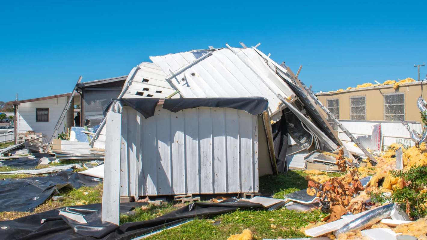 A collapsed mobile home surrounded by debris and scattered insulation materials.