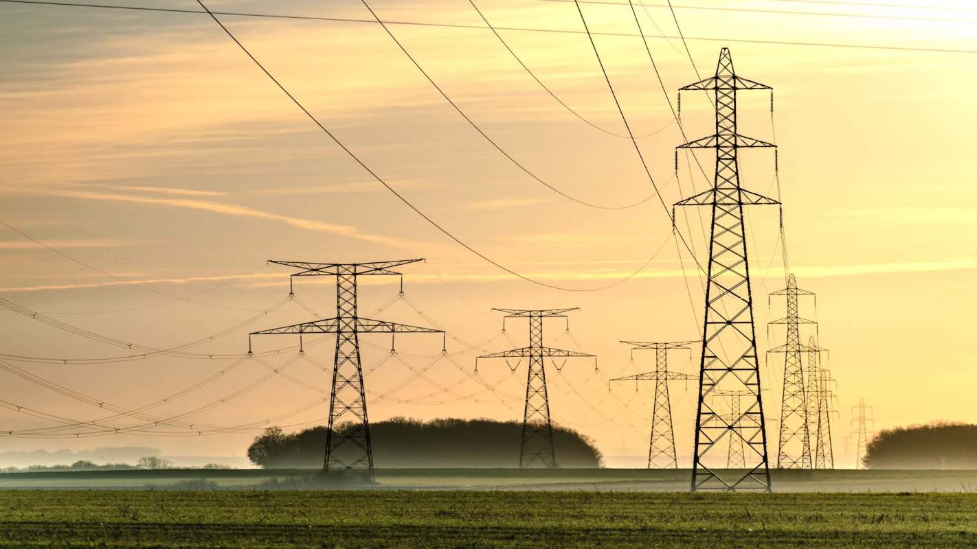 Power lines and transmission towers in a field during sunrise.