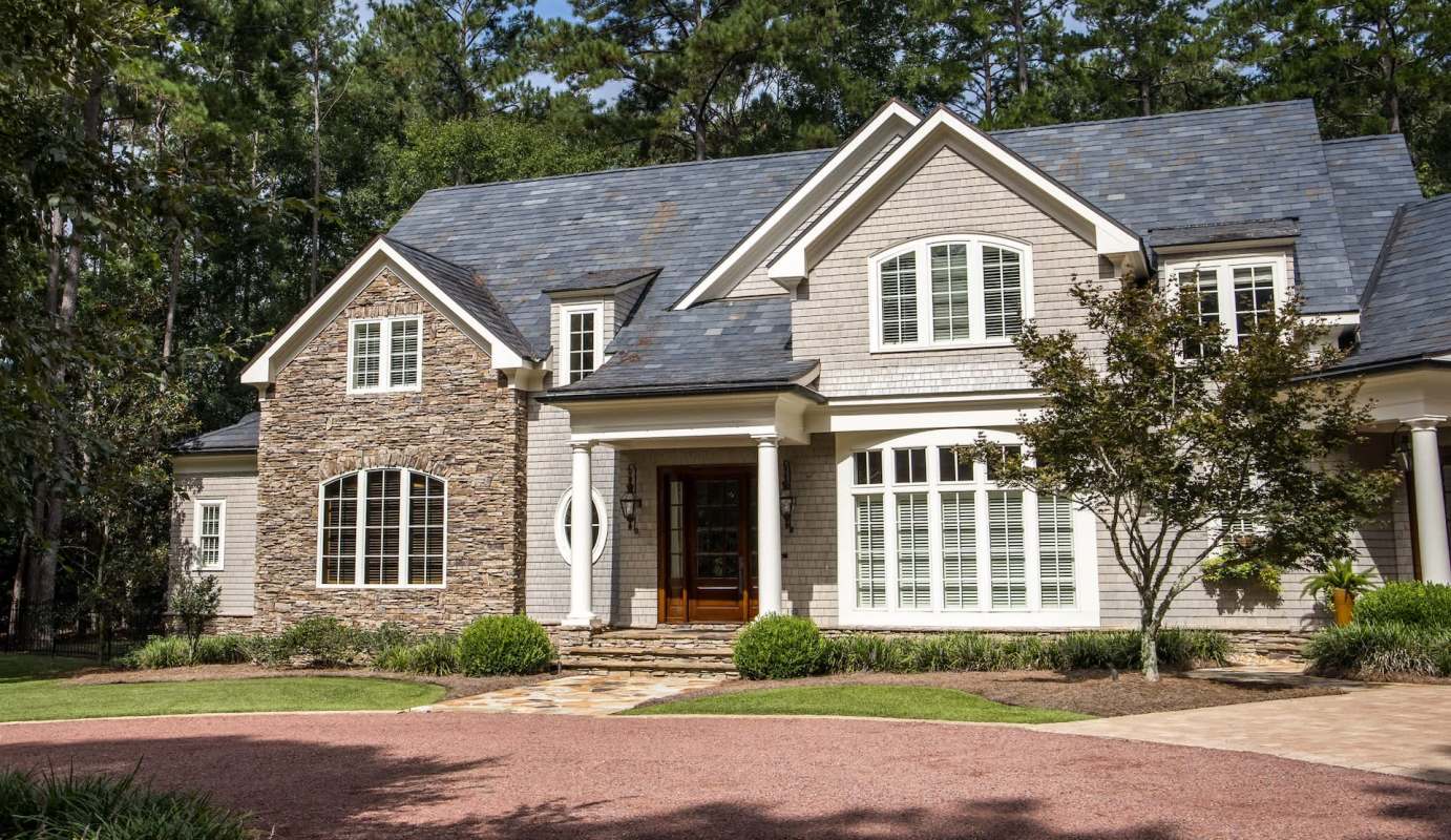 A house with a stone and wood exterior surrounded by trees and landscaping.