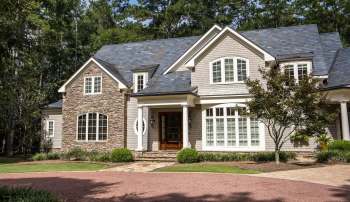 A house with a stone and wood exterior surrounded by trees and landscaping.