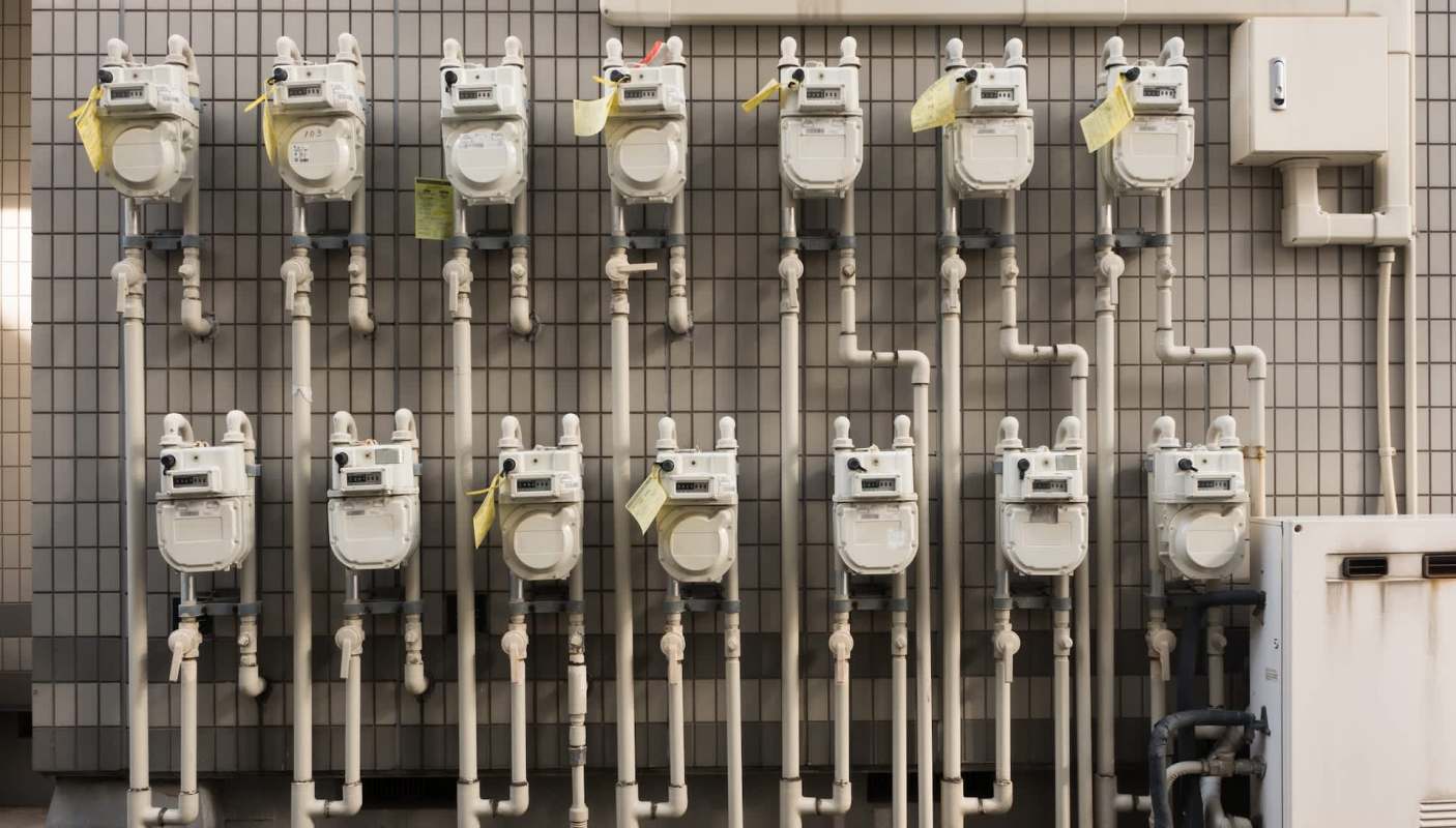 Multiple gas meters installed on a tiled wall with visible pipes and identification tags.