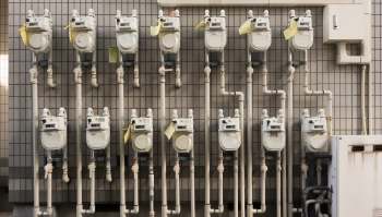 Multiple gas meters installed on a tiled wall with visible pipes and identification tags.