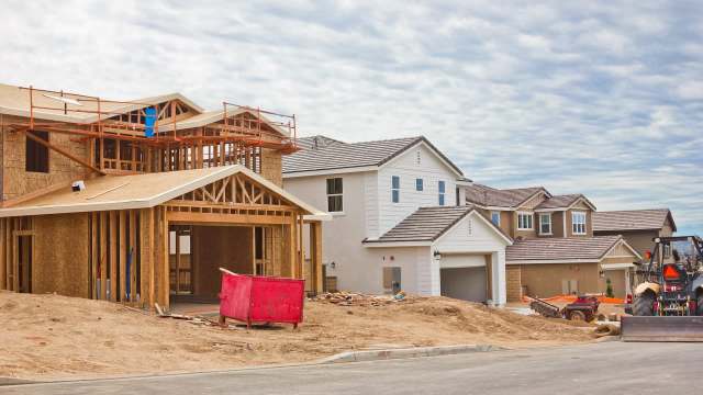 Construction of a new home with scaffolding, nearby completed houses, and construction equipment.