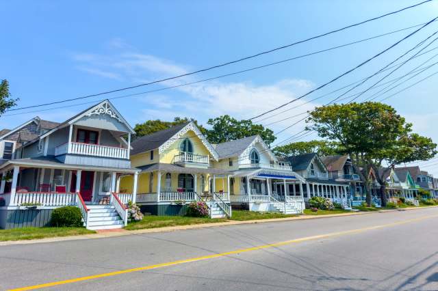 A row of colorful vintage houses with porches along a quiet street under a clear blue sky.