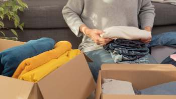 A person folds clothing in front of two boxes filled with assorted garments.