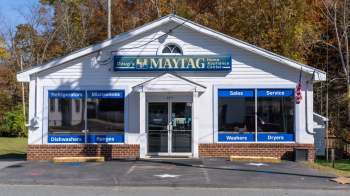 A home appliance store with window displays for refrigerators, microwaves, dishwashers, and other appliances.