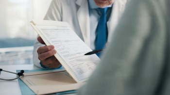 A healthcare professional reviews a medical form while pointing with a pen.