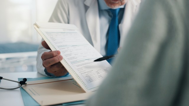 A healthcare professional reviews a medical form while pointing with a pen.