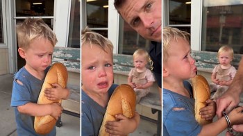 A child holds a large piece of bread while sitting beside a second child and an adult.