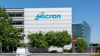 A building with the "Micron" logo and surrounding trees, with a stop sign in the foreground.