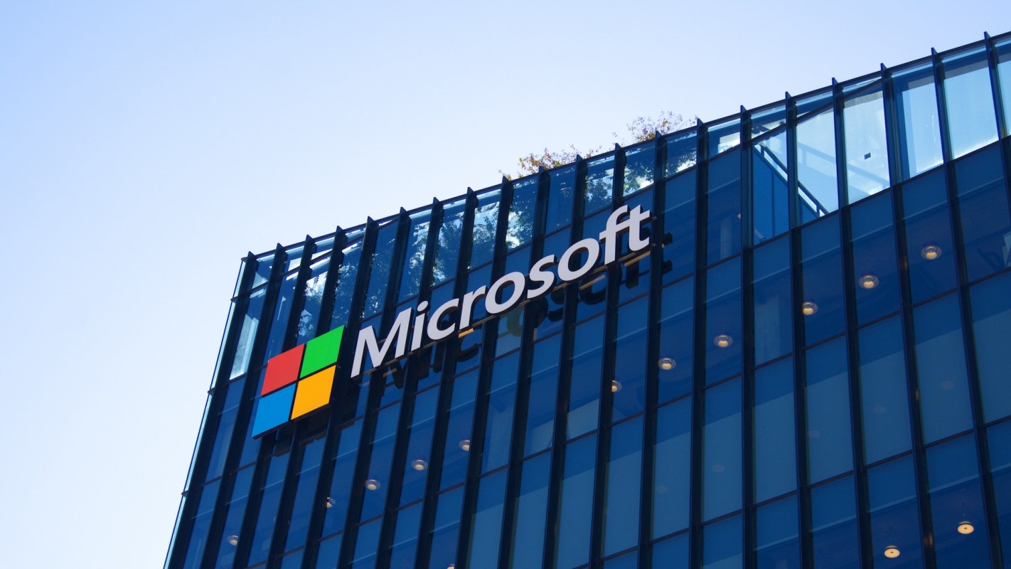 The Microsoft logo displayed on a modern glass building against a clear sky.