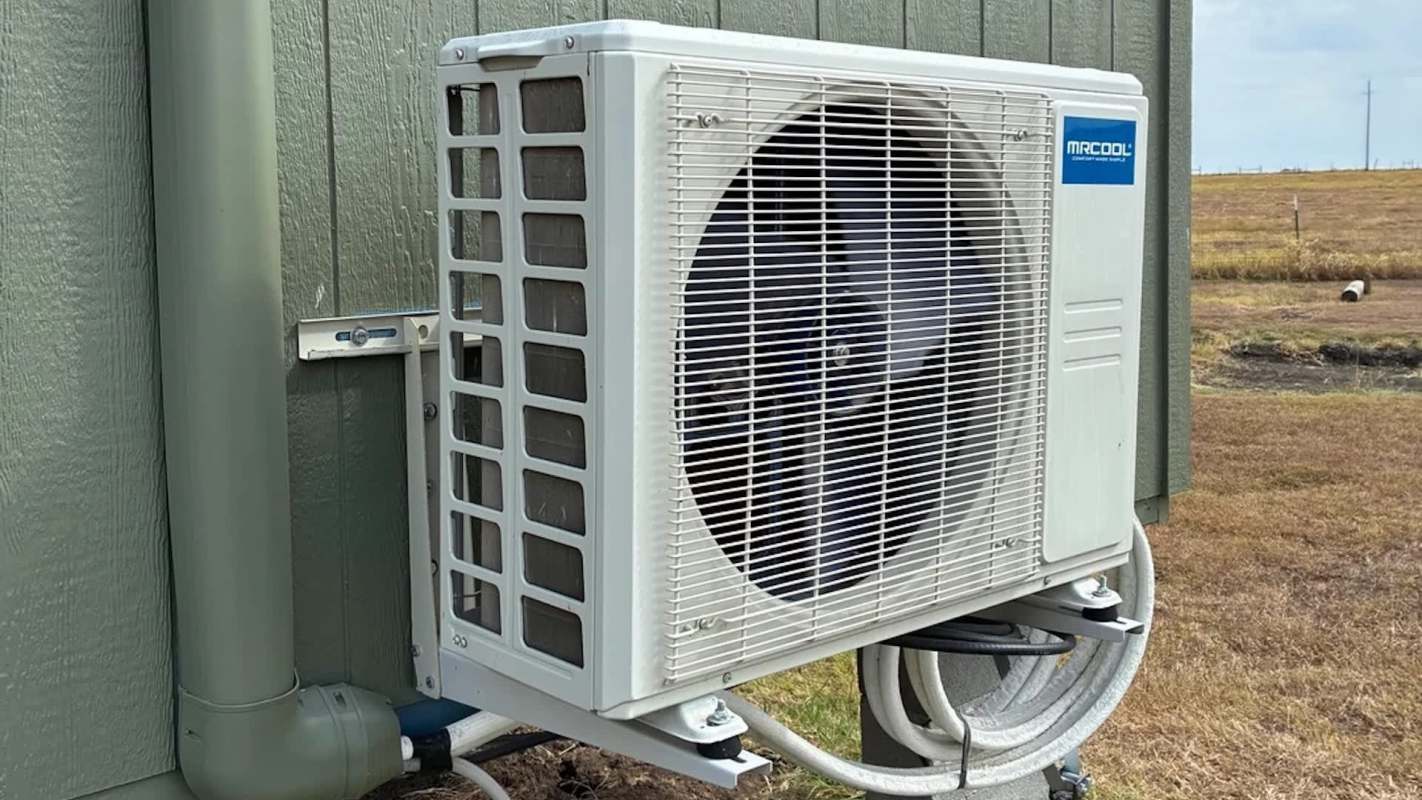 An outdoor air conditioning unit mounted on a wall with pipes nearby.
