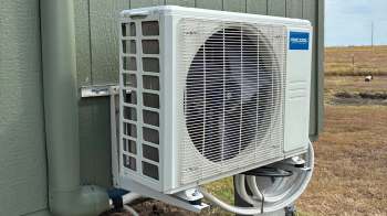An outdoor air conditioning unit mounted on a wall with pipes nearby.