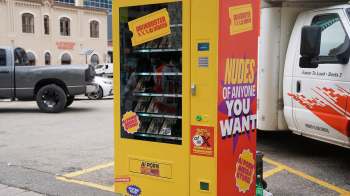 A vending machine advertising adult content, located in a city street.