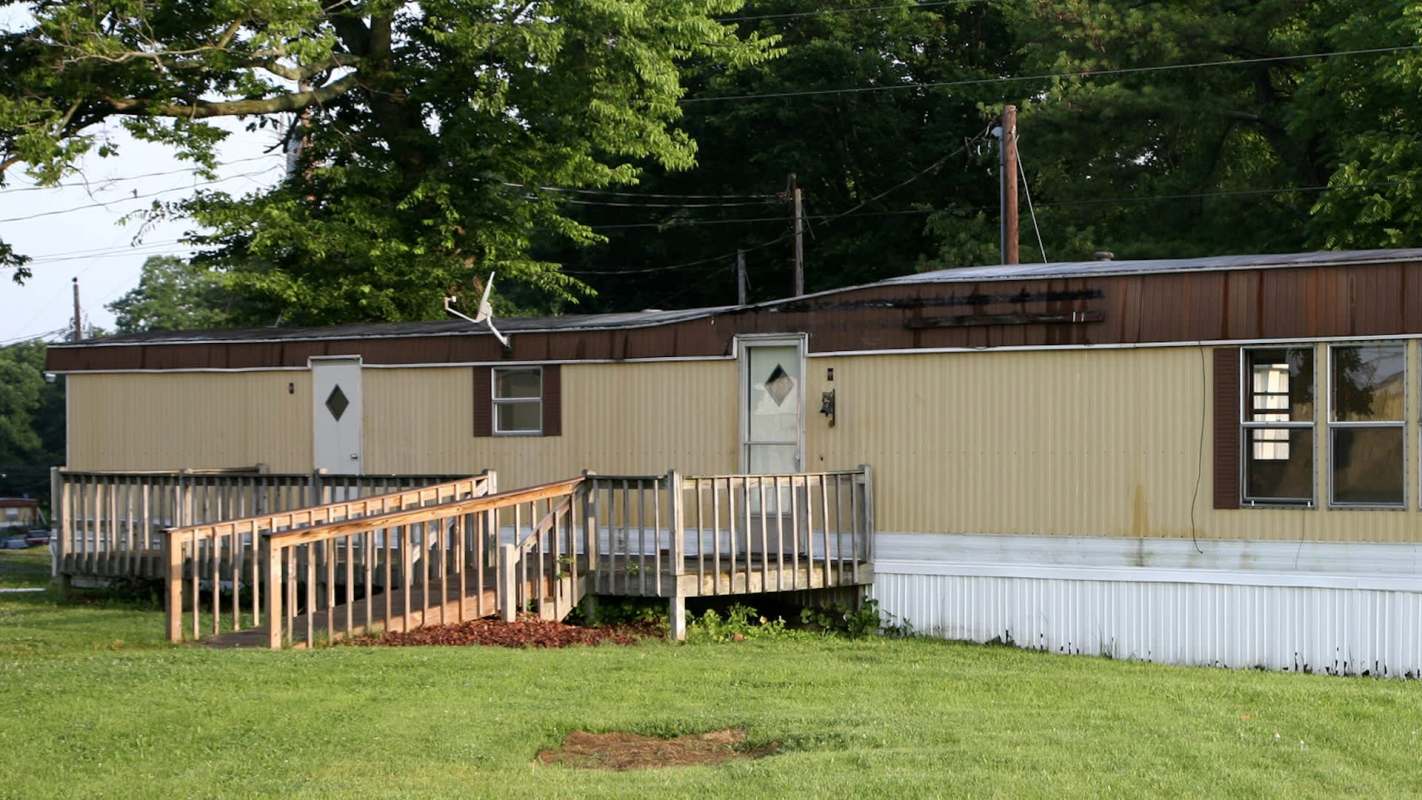 A mobile home with a wooden ramp and grassy area nearby.