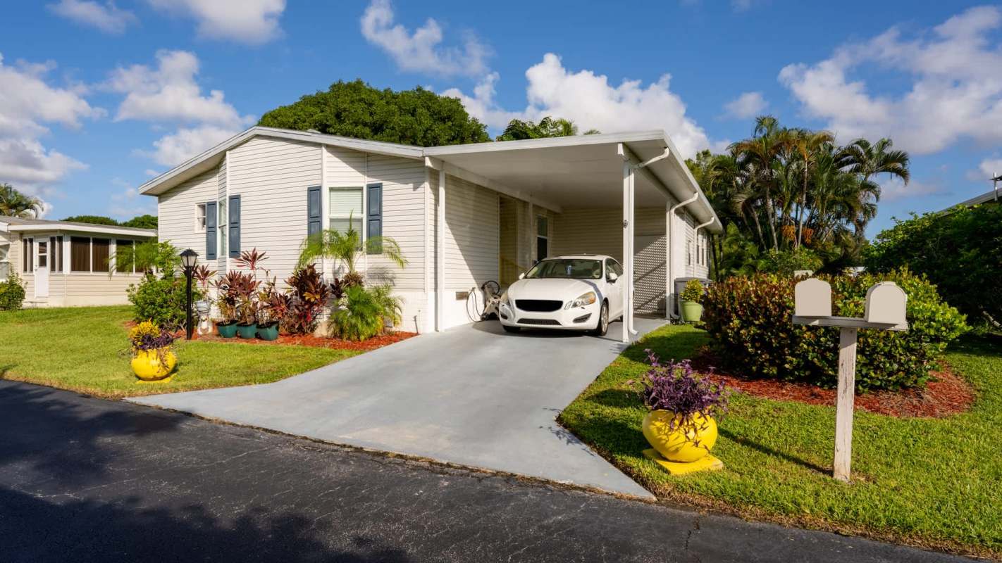 A white car parked in a driveway of a mobile home surrounded by greenery and potted plants.